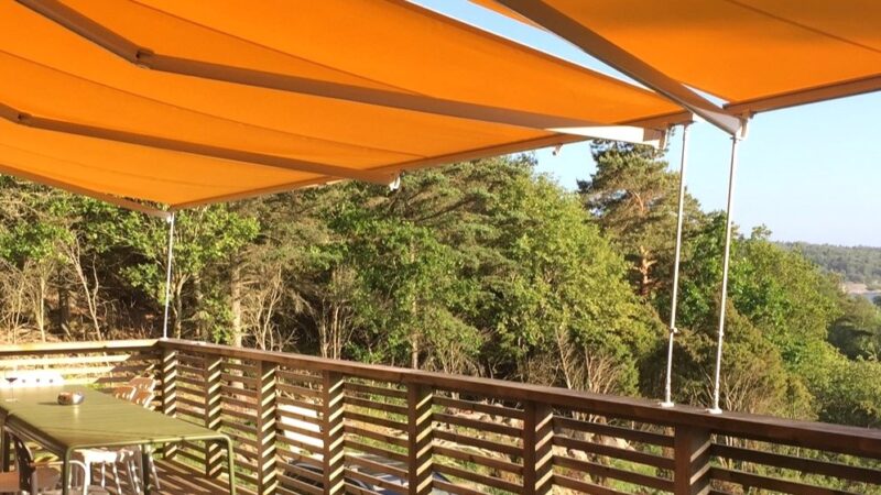 Gula terrassmarkiser med korta vindstag fästa i ett altanräcke