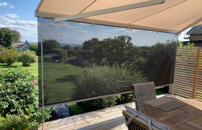 Terrassmarkis med långa vindstag i kombination med hög Sunset screen med genomsikt ut i trädgård