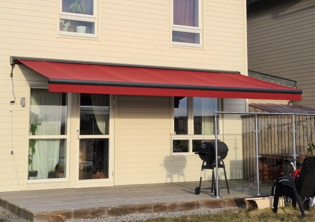 Stor röd terrassmarkis monterad på fasad över terrass