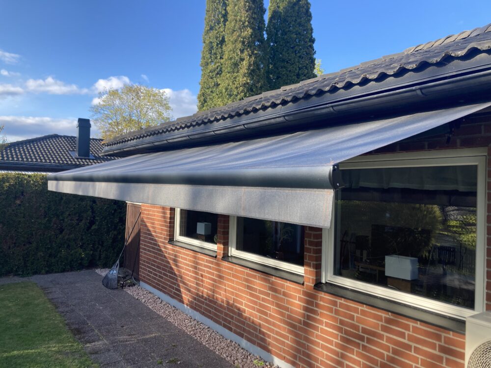 Terrassmarkis i bredd 600cm x armutfall 260cm med Somfy radiomotor samt Somfy skaksensor. Sunflex vinklingsfunktion samt svart lack på armar och profiler. Sandatex markisväv nr. 1330-513 och sydd med orange kontrast tråd enligt kundens önskemål