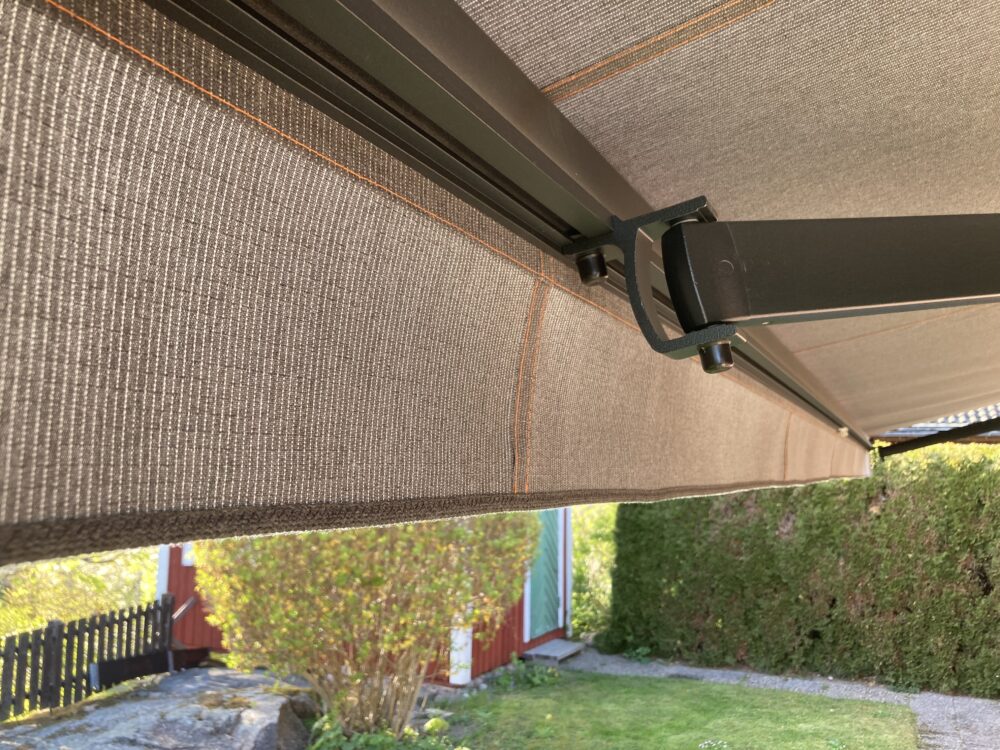 Terrassmarkis i bredd 600cm x armutfall 260cm med Somfy radiomotor samt Somfy skaksensor. Sunflex vinklingsfunktion samt svart lack på armar och profiler. Sandatex markisväv nr. 1330-513 och sydd med orange kontrast tråd enligt kundens önskemål.